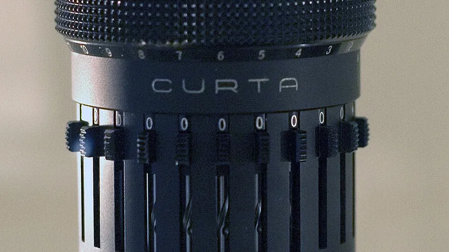 Close-up of a Curta Type II mechanical calculator, showing the CURTA wordmark above the eight setting sliders.