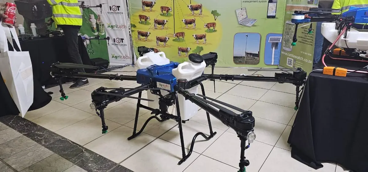 A large agricultural drone with two white tanks on display at a trade stand, Herd-itt cattle posters behind it.